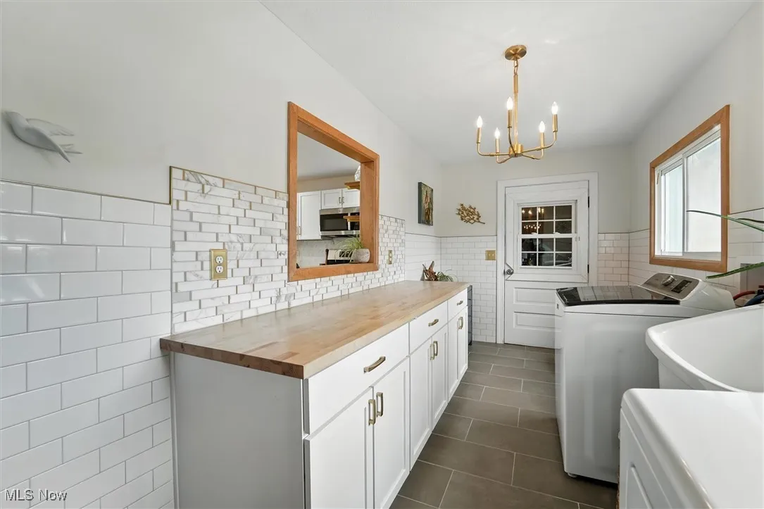 Laundry area featuring cabinet space, a wainscoted wall, washer and clothes dryer, tile walls, and dark tile patterned flooring