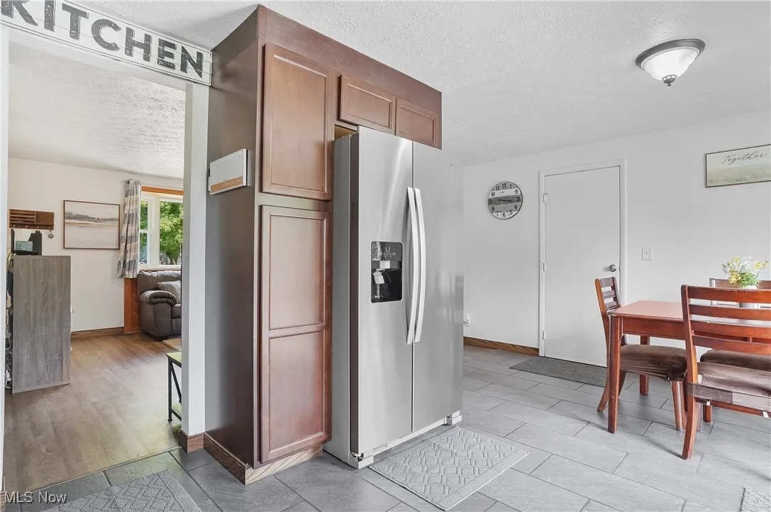 Kitchen featuring stainless steel refrigerator with ice dispenser, a textured ceiling, brown cabinetry, and ceramic tile flooring