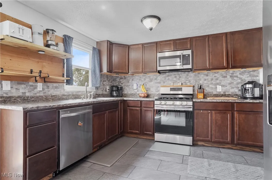 Kitchen featuring open shelves, appliances with stainless steel finishes, backsplash, a  and ceramic tile patterned floors
