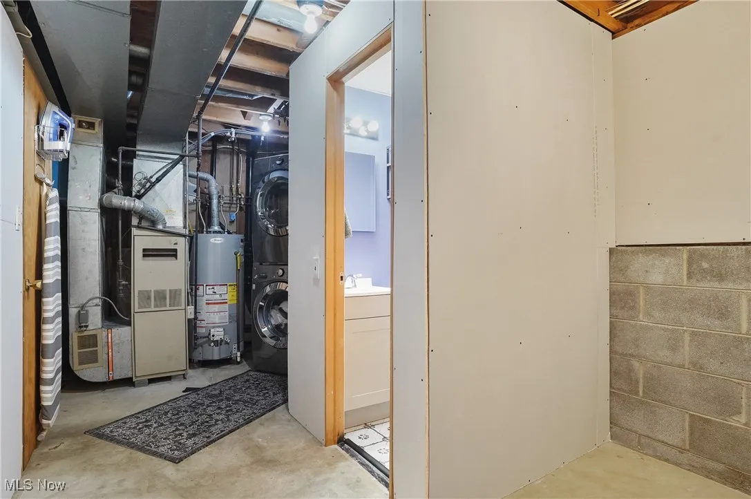 Unfinished basement with stacked washing machine and dryer, gas water heater, and heating unit