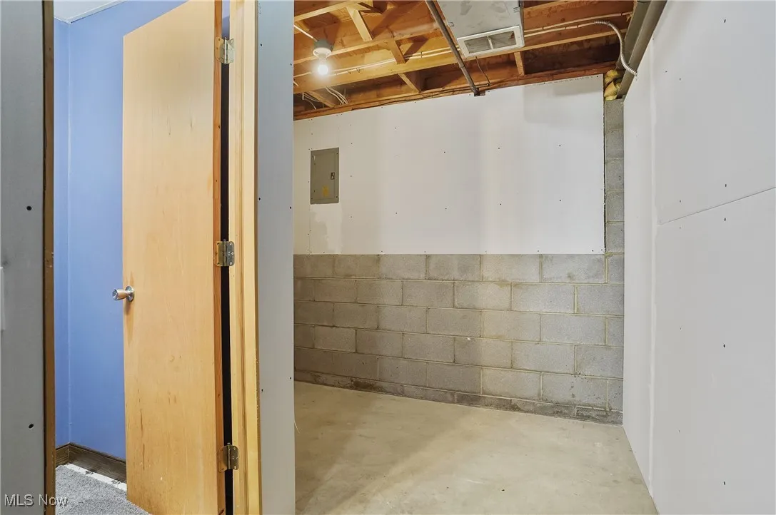 Unfinished basement with concrete block wall and electric panel