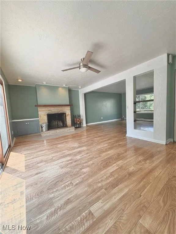 Unfurnished great-room with light wood finished floors, a textured ceiling, a fireplace with raised hearth, and ceiling fan