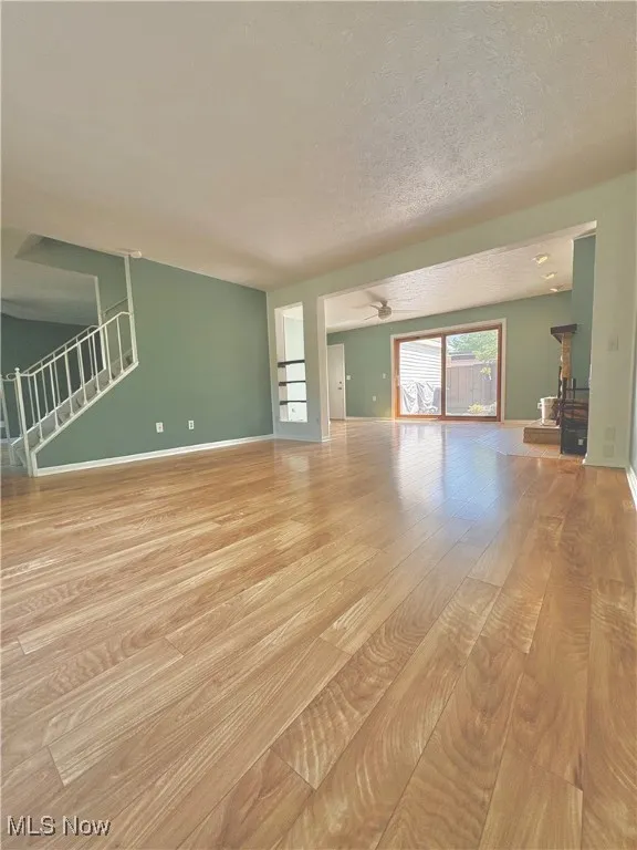 Unfurnished living room with wood finished floors, stairs, a textured ceiling, and a ceiling fan