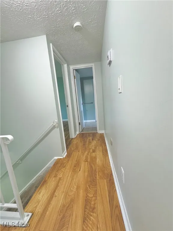 Hallway featuring light wood-style floors, an upstairs landing, and a textured ceiling