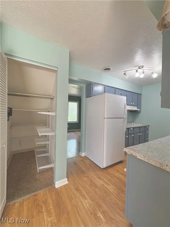 Kitchen featuring a textured ceiling, light wood-style floors, freestanding refrigerator, and light countertops