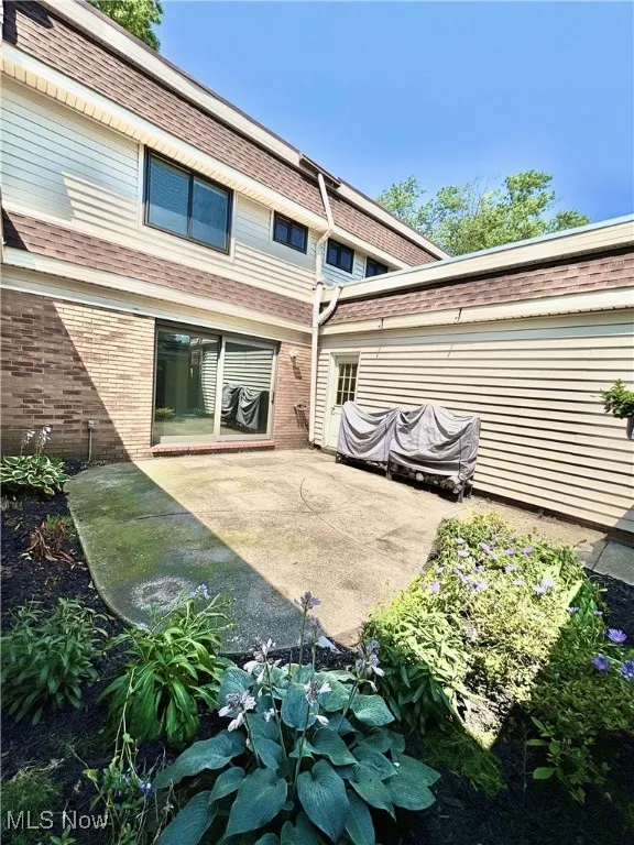 Back of house with brick siding, roof with shingles, a patio area, and mansard roof
