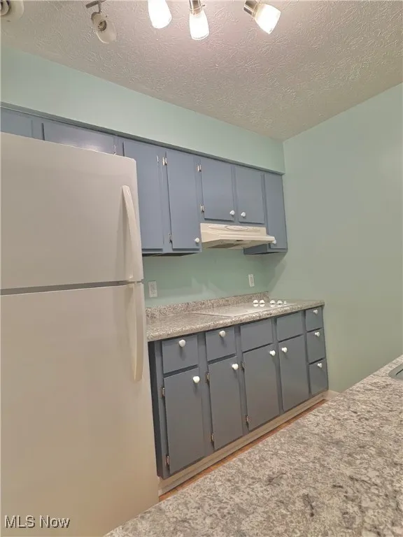 Kitchen featuring white appliances, a textured ceiling, light countertops, gray cabinetry, and under cabinet range hood