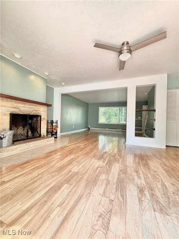Unfurnished great-room featuring a fireplace, a textured ceiling, wood finished floors, a baseboard heating unit, and ceiling fan