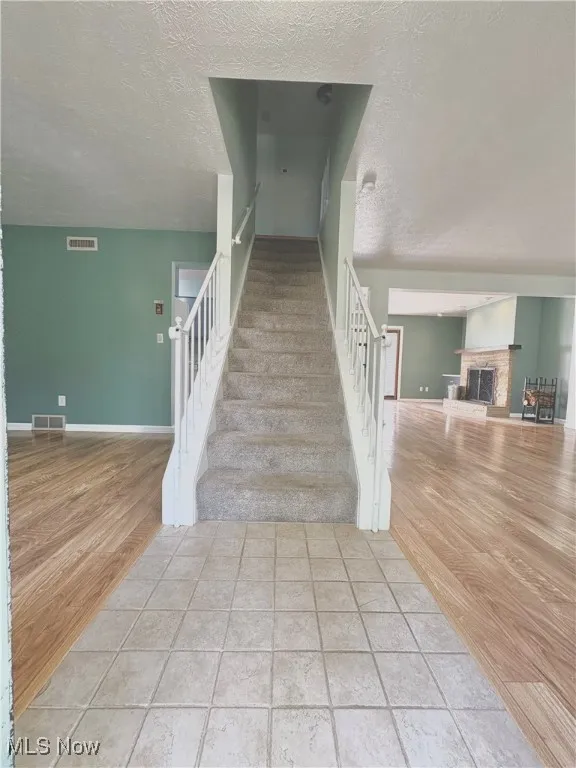 Stairway featuring a textured ceiling, a fireplace with raised hearth, and wood finished floors