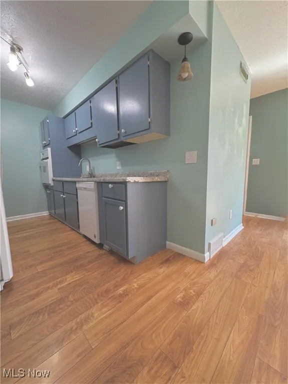 Kitchen featuring a textured ceiling, light wood-style flooring, white appliances, light countertops, and gray cabinets