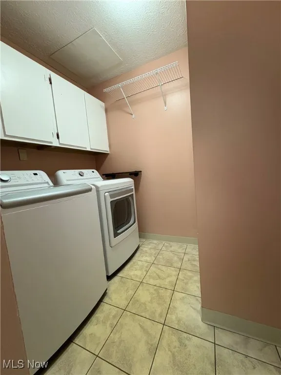 Washroom with independent washer and dryer, cabinet space, light tile patterned flooring, and a textured ceiling