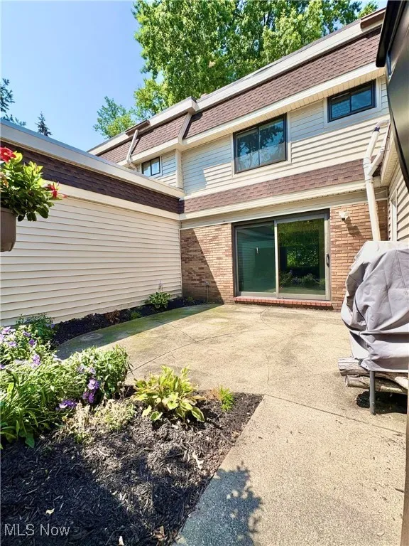Rear view of house with a patio, brick siding, and roof with shingles