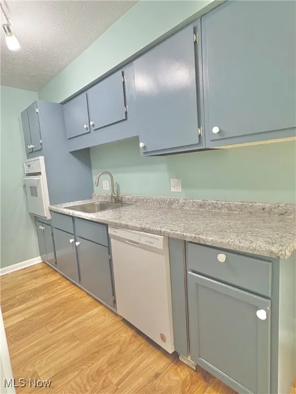 Kitchen with a textured ceiling, light wood-type flooring, white appliances, and light countertops