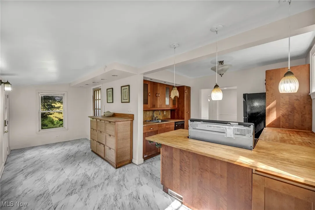 Kitchen with butcher block counters, brown cabinets, decorative light fixtures, light marble finish flooring, and a peninsula
