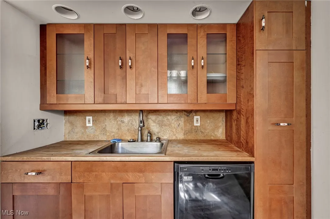 Kitchen featuring black dishwasher, decorative backsplash, glass insert cabinets, and butcher block counters