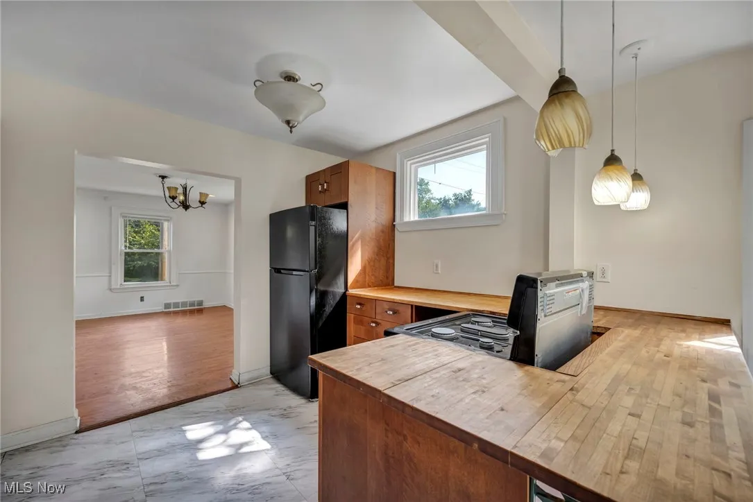 Kitchen with freestanding refrigerator, light marble finish flooring, brown cabinetry, and decorative light fixtures