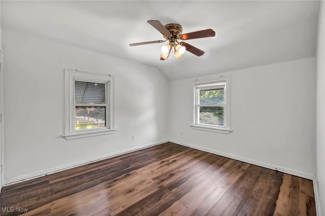 Spare room featuring dark wood finished floors, lofted ceiling, and ceiling fan