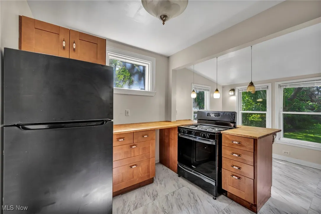 Kitchen with black appliances, brown cabinets, wooden counters, and light marble finish floors