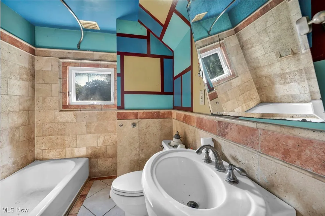 Full bathroom featuring a tub to relax in, tile patterned floors, and tile walls