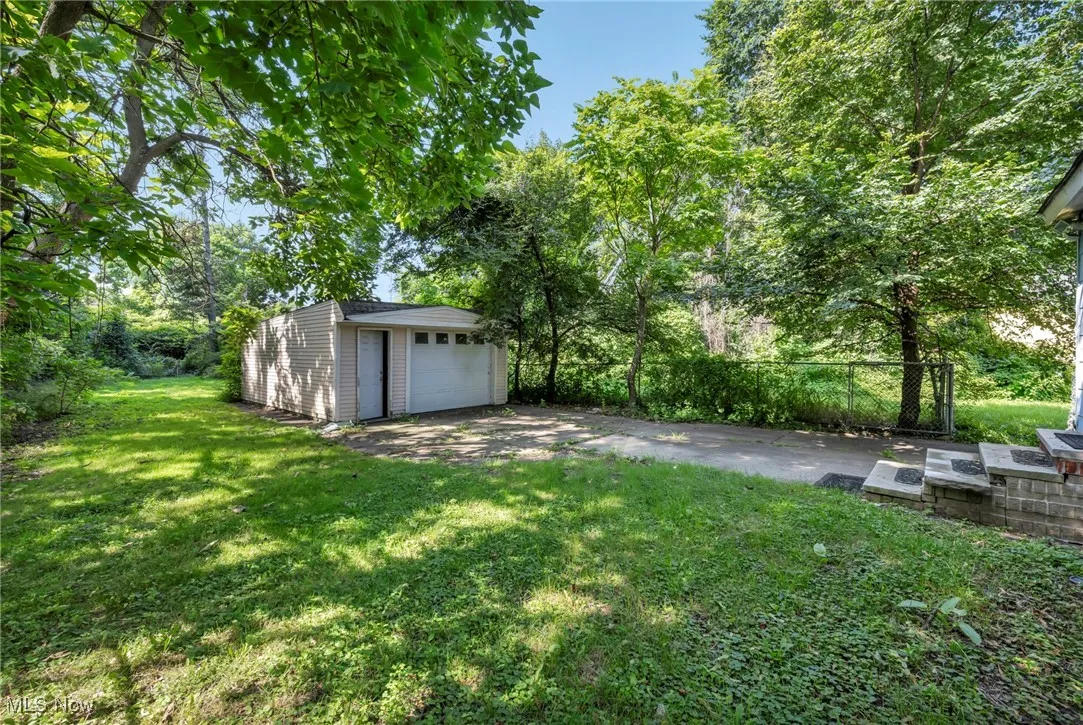 View of grassy yard with an outdoor structure, a detached garage, and view of wooded area