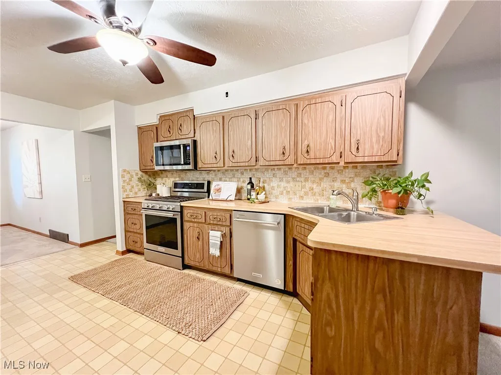 Kitchen featuring stainless steel appliances, backsplash, light countertops, a textured ceiling, and ceiling fan