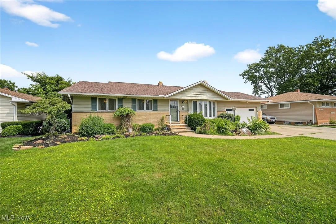 Ranch-style home featuring a front yard, driveway, brick siding, an attached garage, and a chimney