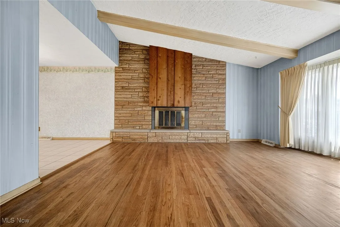 Living Room featuring wood finished floors, a stone fireplace, and a textured cathedral ceiling.
