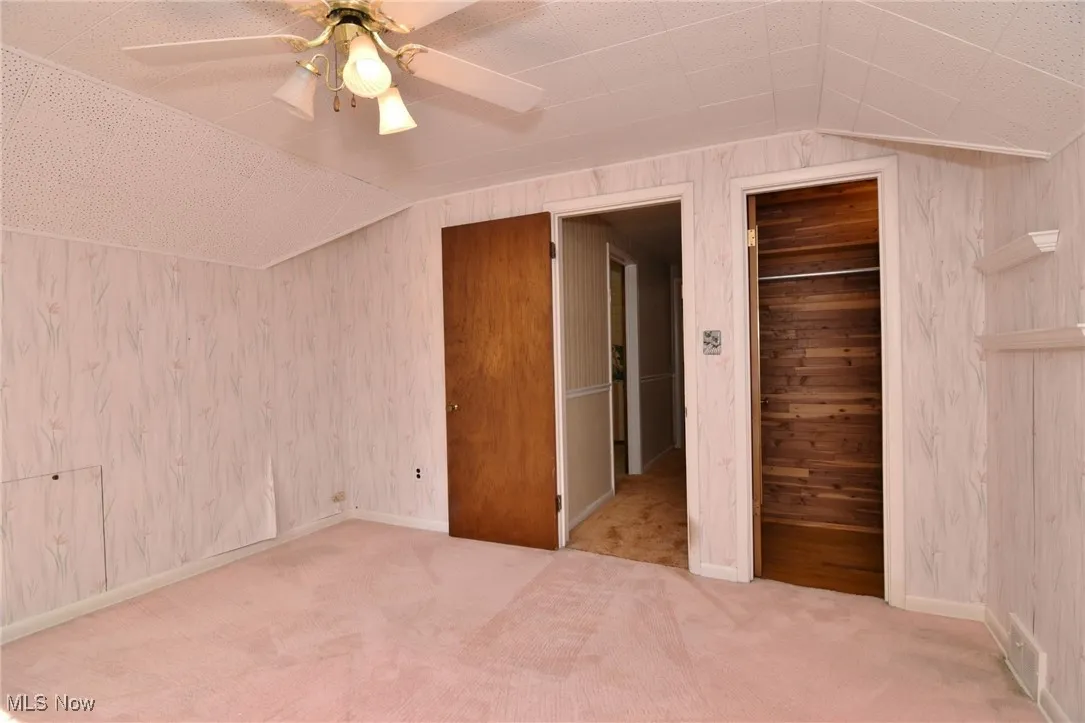 Bedroom #3, upstairs. Featuring lofted ceiling, carpet flooring, wooden walls, a ceiling fan, and a cedar closet.