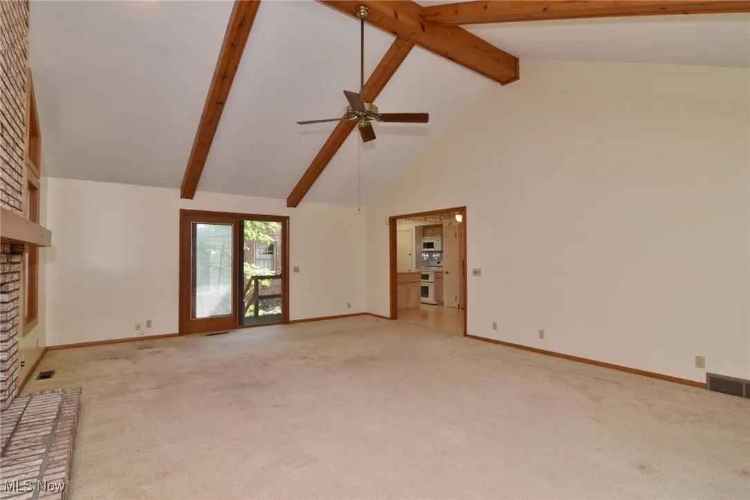 View from far wall. Featuring light colored carpet, beamed ceiling, a fireplace, high vaulted ceiling, and ceiling fan