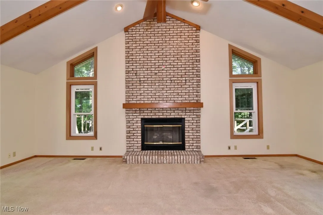 Featuring beamed ceiling, carpet flooring, a ventless gas fireplace, and high vaulted ceiling