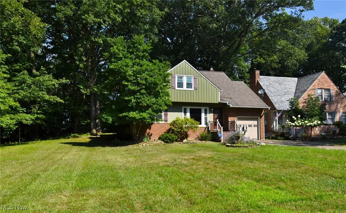 View of front facade with brick siding, a chimney, a front yard, and driveway