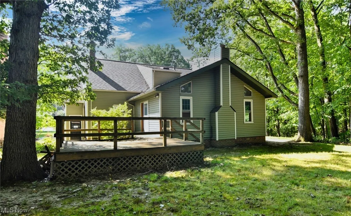 Rear view of house with a chimney, a lawn, a deck, and roof with shingles