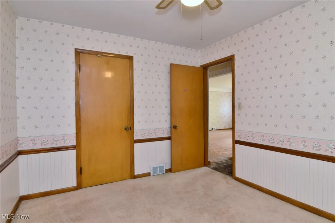 Bedroom #2, main floor, with wallpapered walls, carpet floors, ceiling fan, and wainscoting