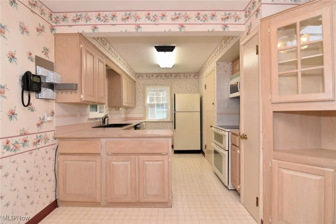 Kitchen with built-ins, appliances, light brown cabinets, light floors, and light countertops