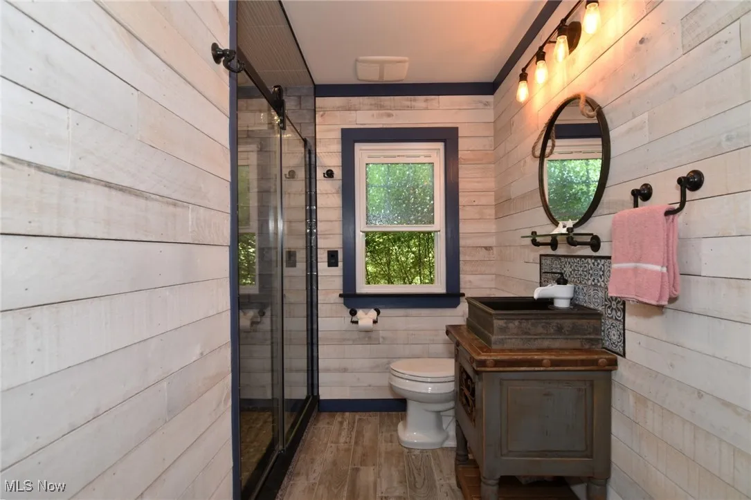 Full bathroom on main floor featuring wooden walls, wood finished floors, vanity, shower, and one wimdow