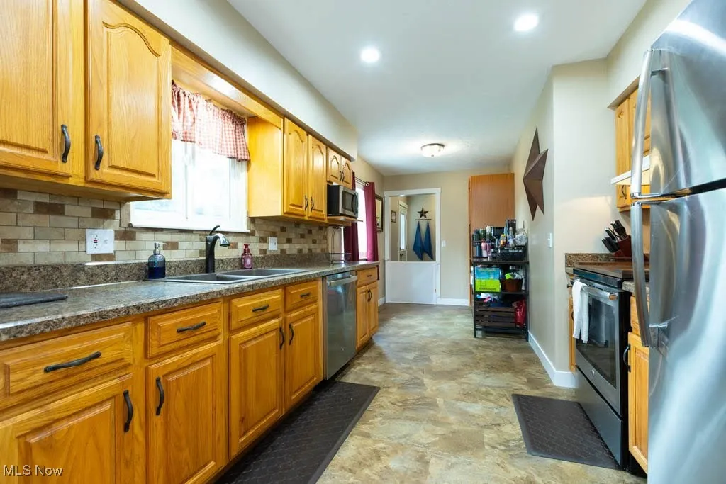 Kitchen with tasteful backsplash, appliances with stainless steel finishes, dark countertops, brown cabinetry, and stone finish floors