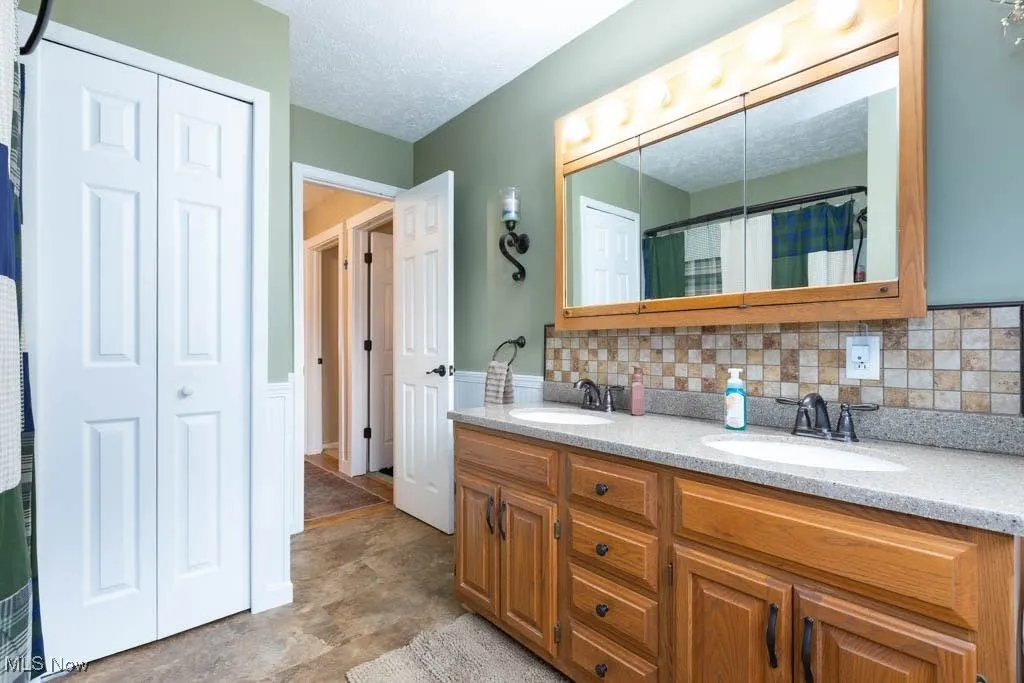 Bathroom featuring double vanity, wainscoting, a textured ceiling, a shower with shower curtain, and decorative backsplash