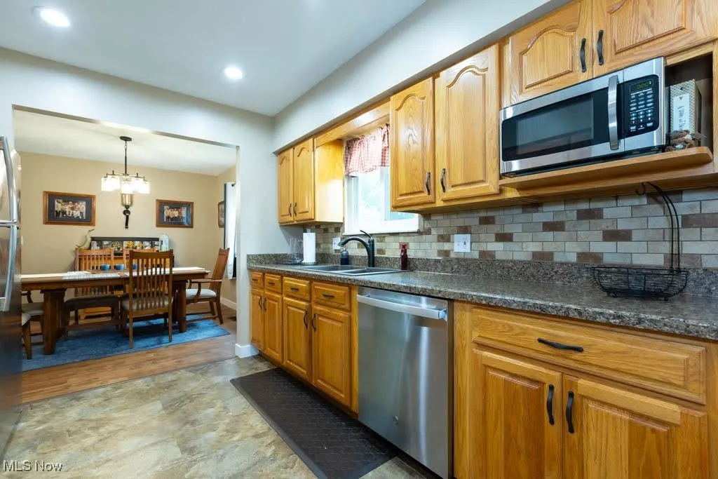 Kitchen with stainless steel appliances, backsplash, a chandelier, decorative light fixtures, and brown cabinetry