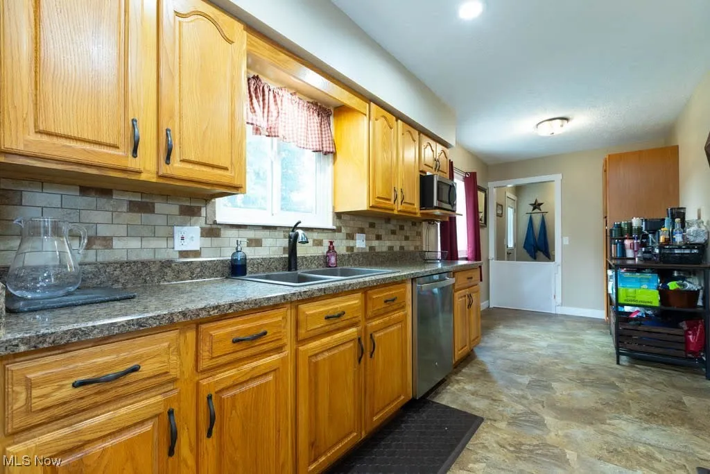 Kitchen featuring tasteful backsplash, appliances with stainless steel finishes, dark countertops, stone finish floors, and brown cabinetry