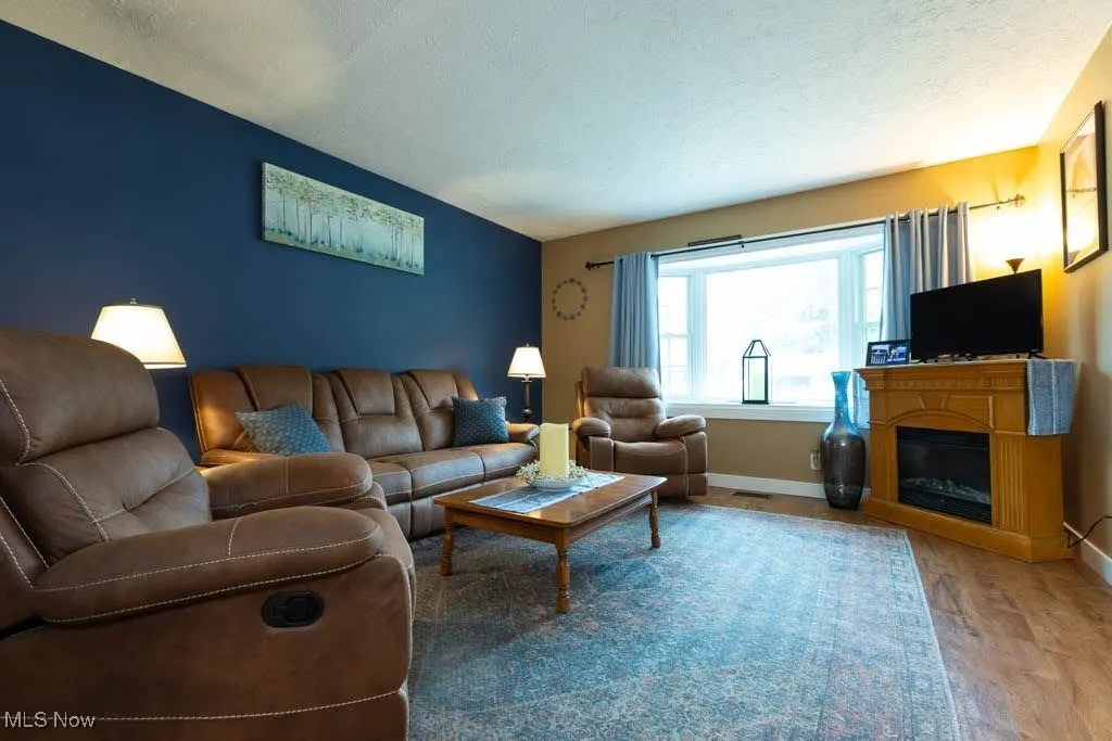 Living area with light wood-style flooring, a textured ceiling, and a glass covered fireplace