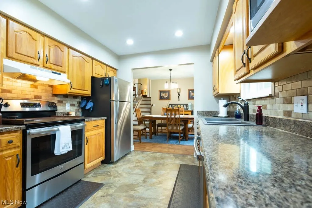 Kitchen featuring backsplash, appliances with stainless steel finishes, under cabinet range hood, dark countertops, and recessed lighting