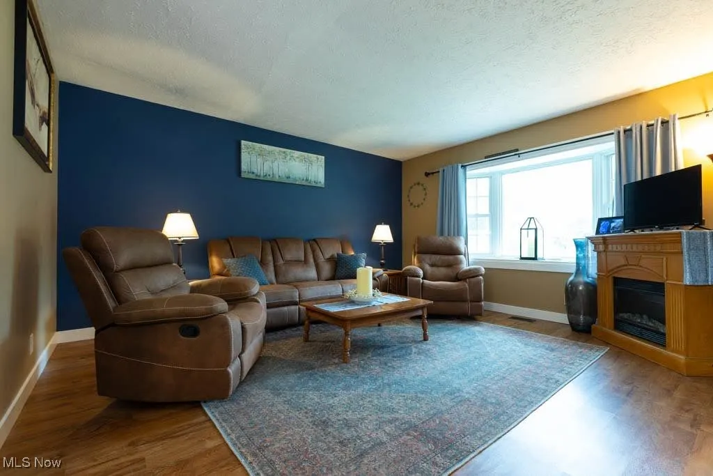 Living area featuring wood finished floors, a textured ceiling, and a glass covered fireplace