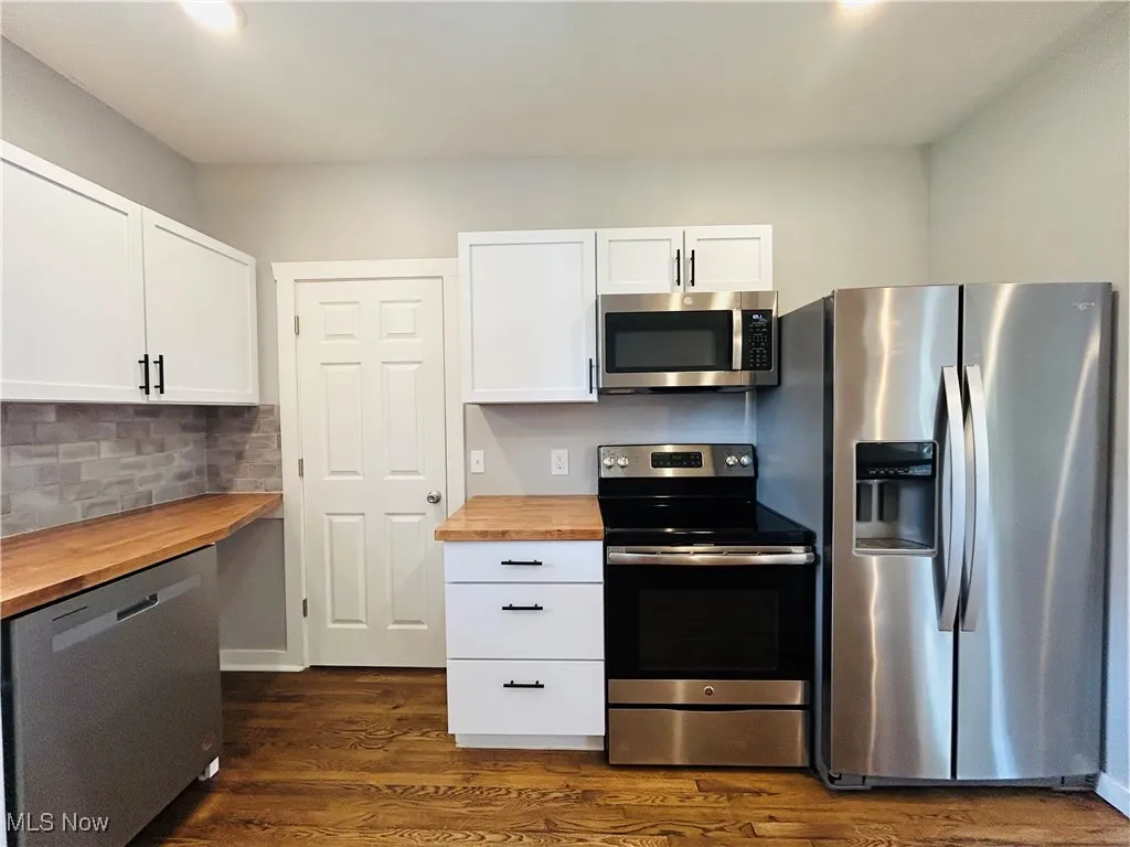 Kitchen with butcher block countertops, appliances with stainless steel finishes, dark wood-style floors, white cabinets, and tasteful backsplash