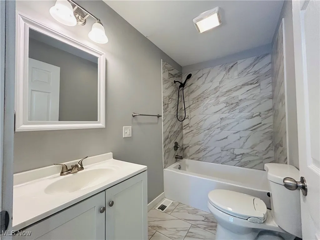 Full bathroom featuring marble finish floors, vanity, and washtub / shower combination