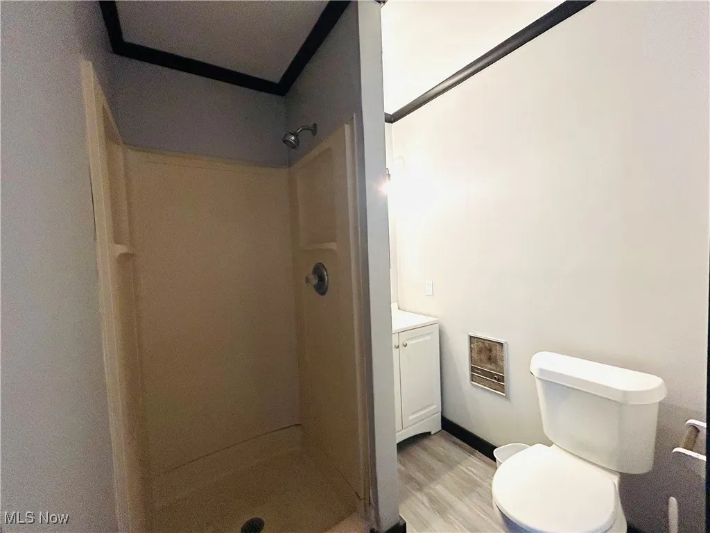 Full bathroom with a shower stall, vanity, wood finished floors, and heating unit, additional living suite