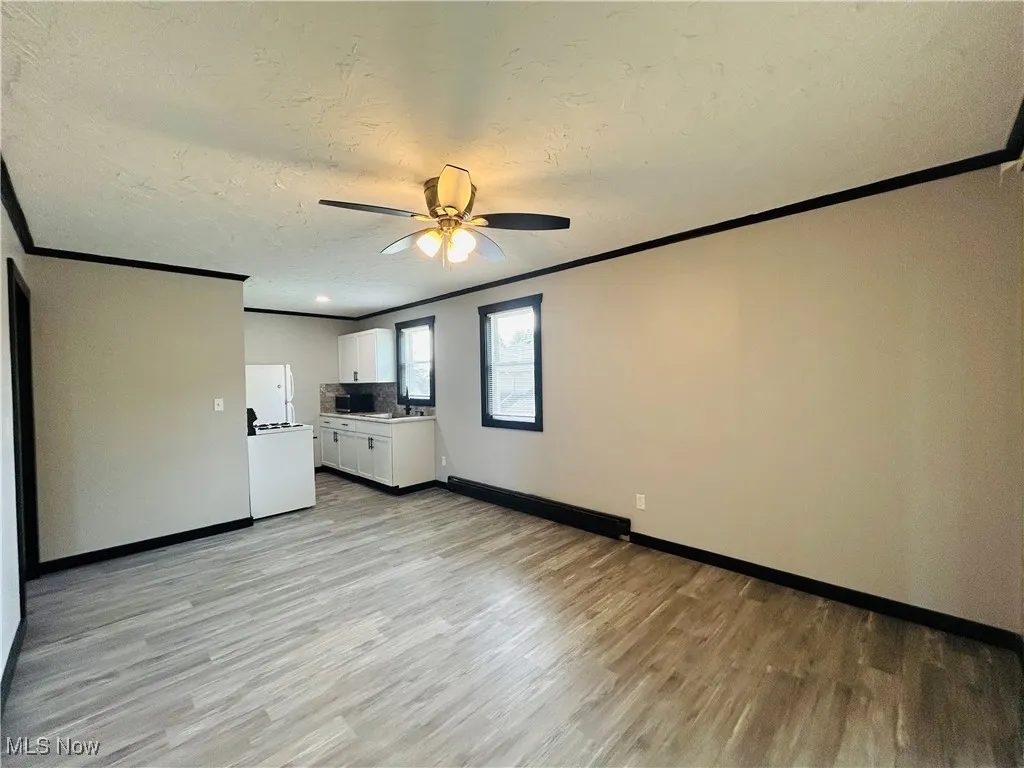 Unfurnished living room featuring crown molding, a textured ceiling, light wood-style floors, and ceiling fan, Additional living suite.