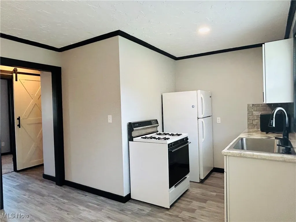 Kitchen featuring a barn door, white appliances, light wood-style floors, white cabinetry, and light countertops, additional living suite.
