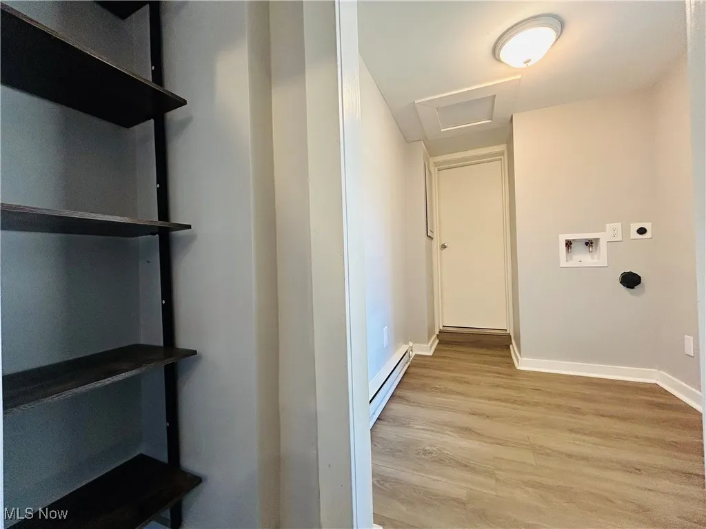 Corridor featuring attic access, light wood-style floors, and a baseboard radiator