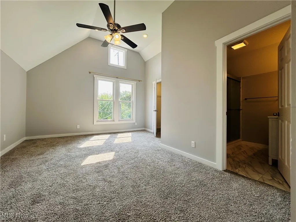 Unfurnished bedroom with carpet flooring, ceiling fan, and high vaulted ceiling