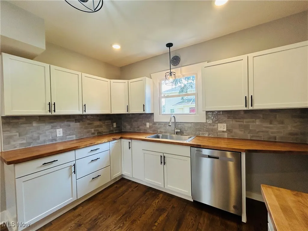 Kitchen featuring butcher block countertops, dishwasher, dark wood-style flooring, white cabinetry, and pendant lighting